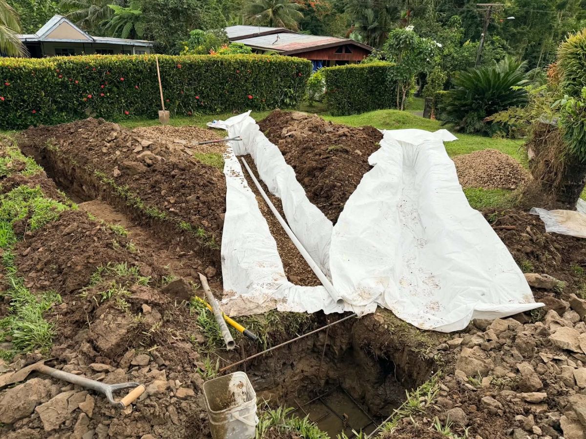 Trench lined with geotextile and gravel around the distribution pipe; reinforcement set in the pit